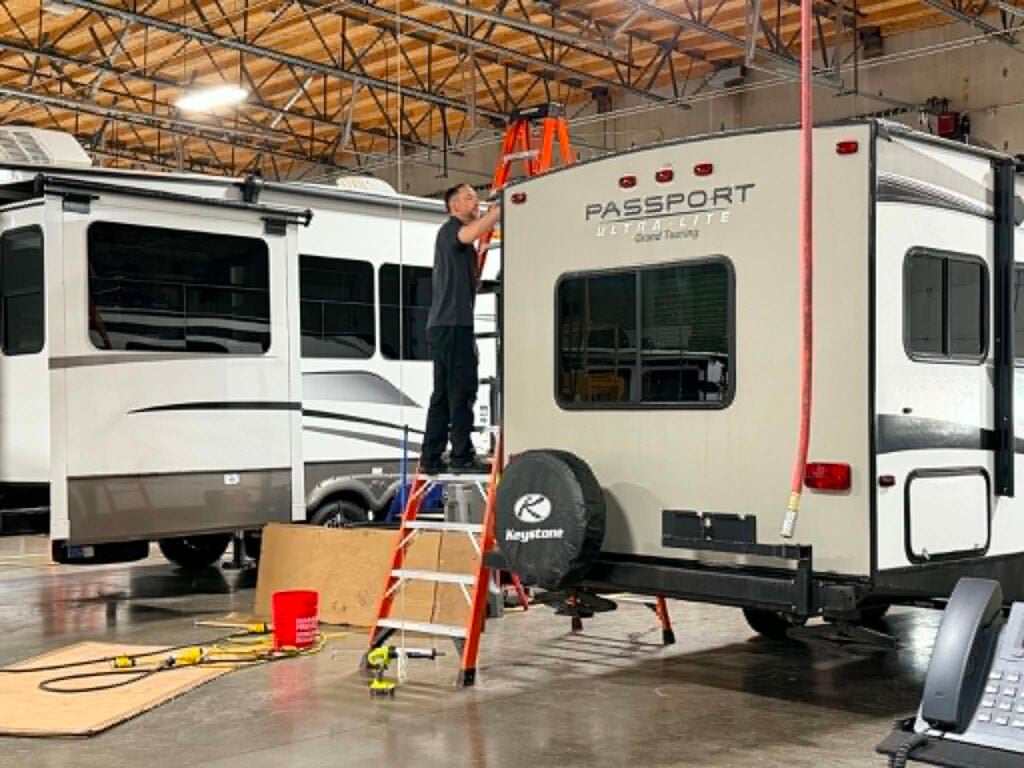 Technician inspecting and servicing an RV roof during spring maintenance preparation for summer camping in Washington.