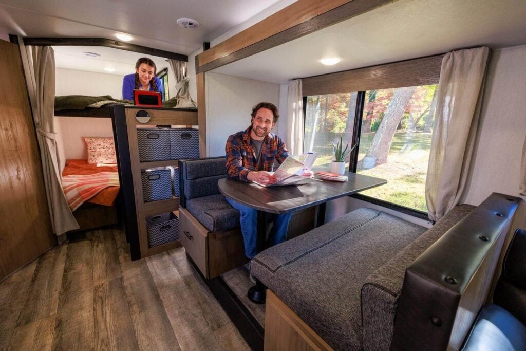 Family relaxing inside a travel trailer RV with bunk beds and dinette, showcasing comfortable RV living for camping trips in Washington state.