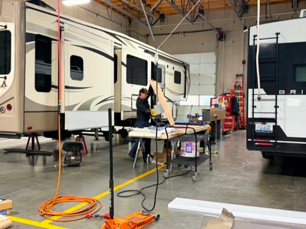 RV technician performing spring maintenance and repairs on a fifth wheel trailer inside Tacoma RV’s service center before summer camping season.