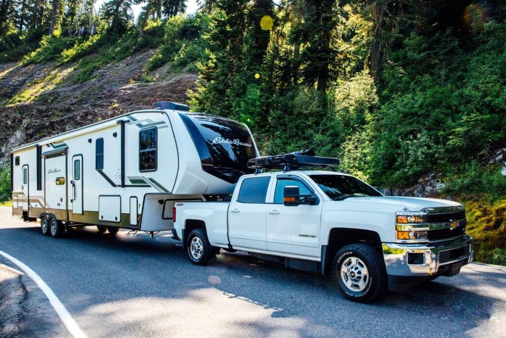 Heavy-duty truck towing a large fifth wheel RV through forest mountain roads near Mount Rainier while demonstrating proper towing capacity and hitch setup.