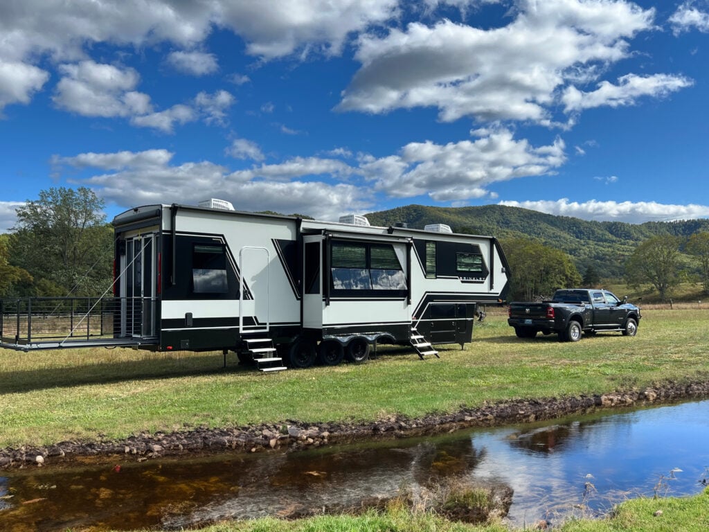 Couple relaxing outside a modern fifth wheel camper at a wooded campground, highlighting comfortable RV living and family-friendly camping for new RV owners.