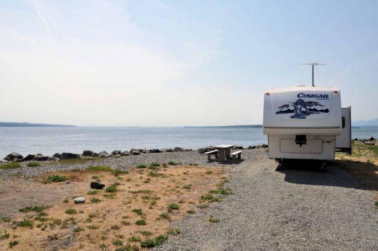 Waterfront RV camping site overlooking Puget Sound with a fifth wheel trailer parked beside the beach, showcasing scenic oceanfront campgrounds in Washington State for Summer 2026.