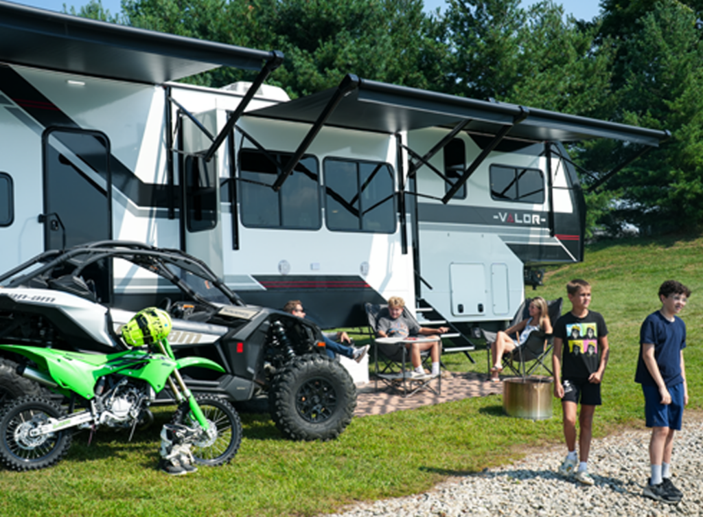 Family enjoying a campground stay beside a toy hauler RV with off-road vehicles, showcasing adventure-focused RV camping and versatile options for first-time RV buyers seeking outdoor travel and recreation 