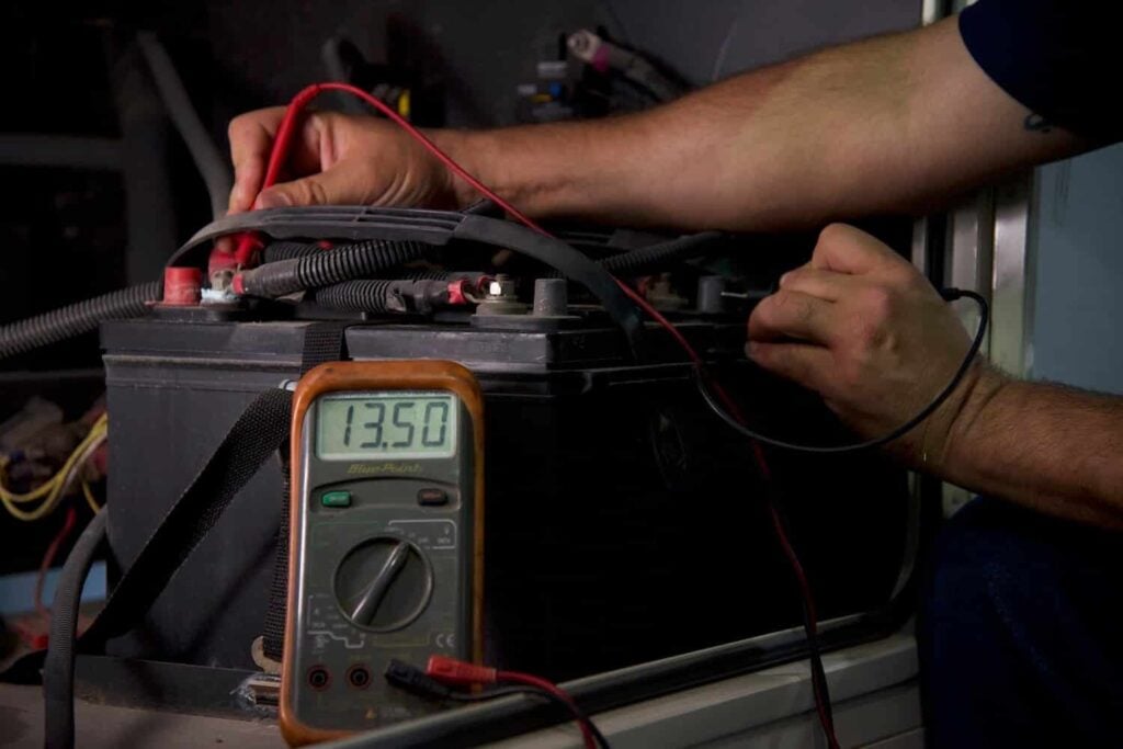 Technician testing RV battery voltage during a spring RV maintenance inspection before Pacific Northwest summer camping season.