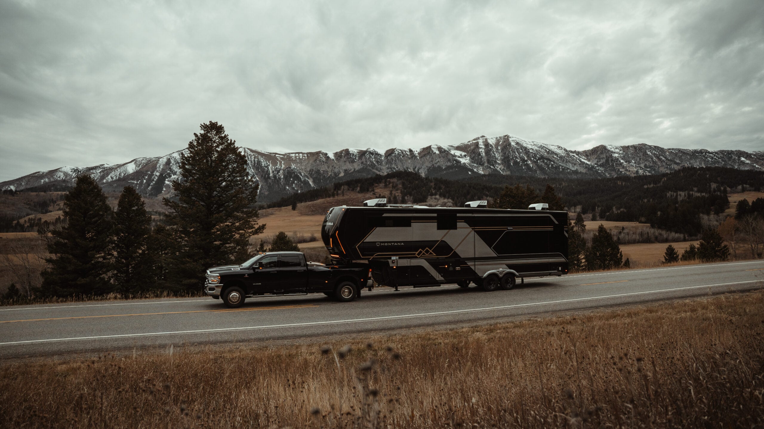 Luxury Montana fifth wheel RV being towed by a heavy-duty pickup truck on a mountain highway under cloudy skies.