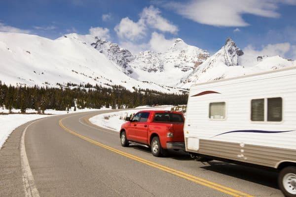 Travel trailer being towed by a red pickup truck along a snowy mountain road during an RV road trip adventure.