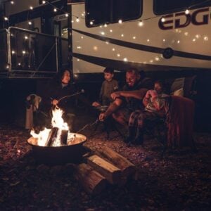 Family gathered around a campfire outside their RV at night, enjoying quality time and outdoor camping experiences in a family-friendly RV.