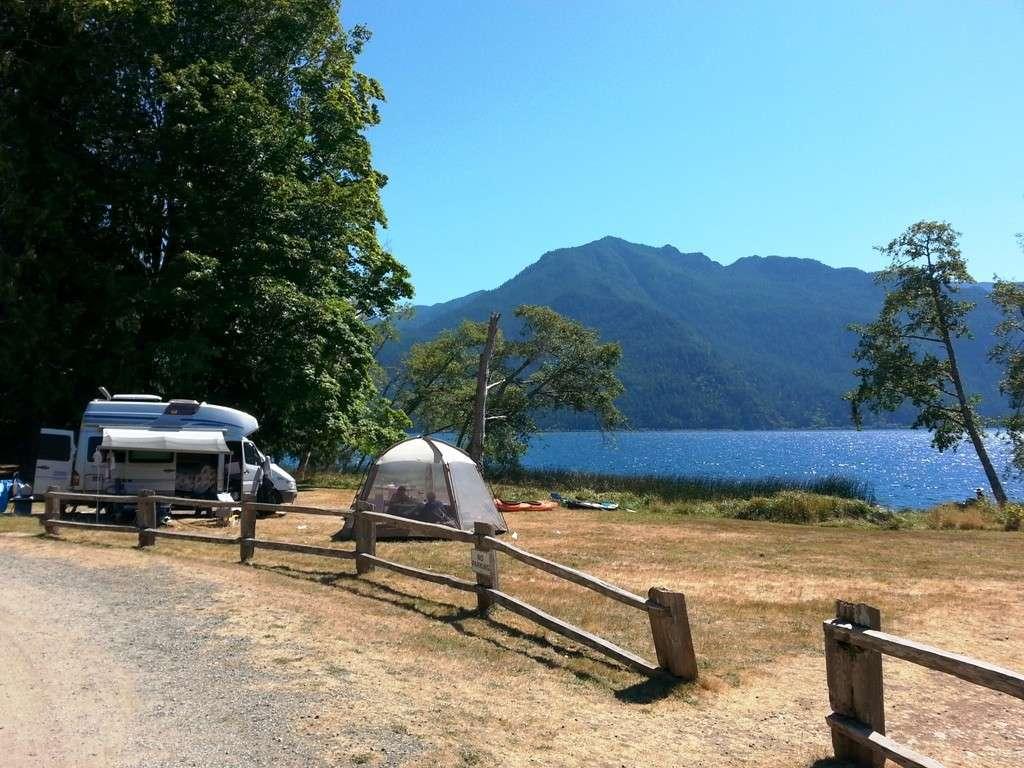 RV and tent campsite beside a scenic mountain lake in Washington State with forest views and calm blue water on a sunny day.