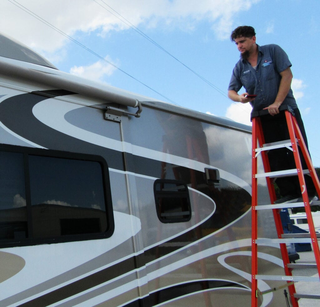 RV technician inspecting a fifth wheel roof and awning during a spring RV maintenance inspection to prepare for PNW summer camping adventures.