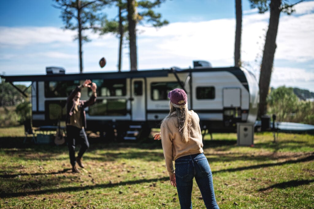 Couple playing catch outside a travel trailer at a forest campsite, enjoying outdoor RV camping lifestyle in Washington state.
