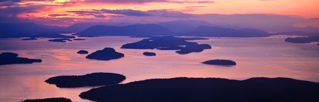Aerial sunset view of the San Juan Islands in Washington State with ocean waterways and forested islands, a top Pacific Northwest destination for RV camping and outdoor adventures.