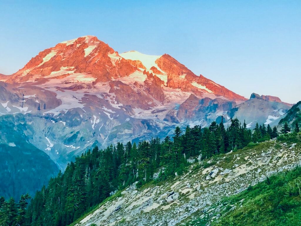 Mount Rainier glowing during sunset with snow-covered peaks and evergreen forests in Washington State, a scenic destination for RV and outdoor adventure travel.