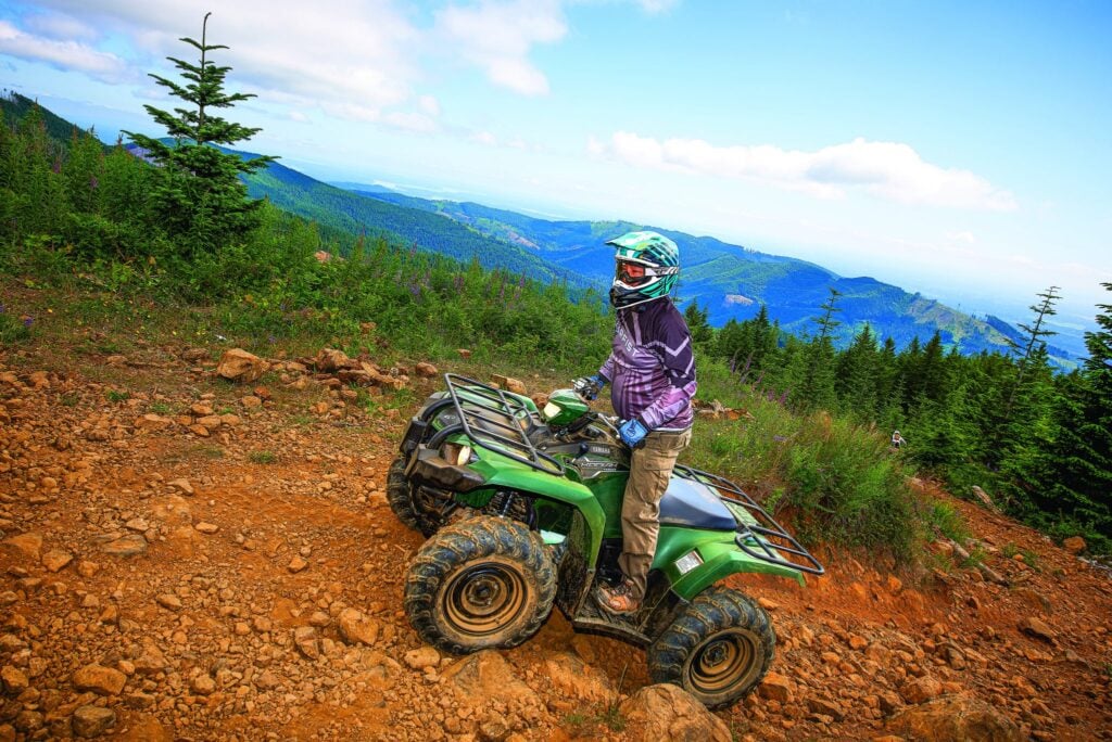 ATV rider overlooking mountain trails and forest scenery in Washington State during an off-road outdoor adventure ride.